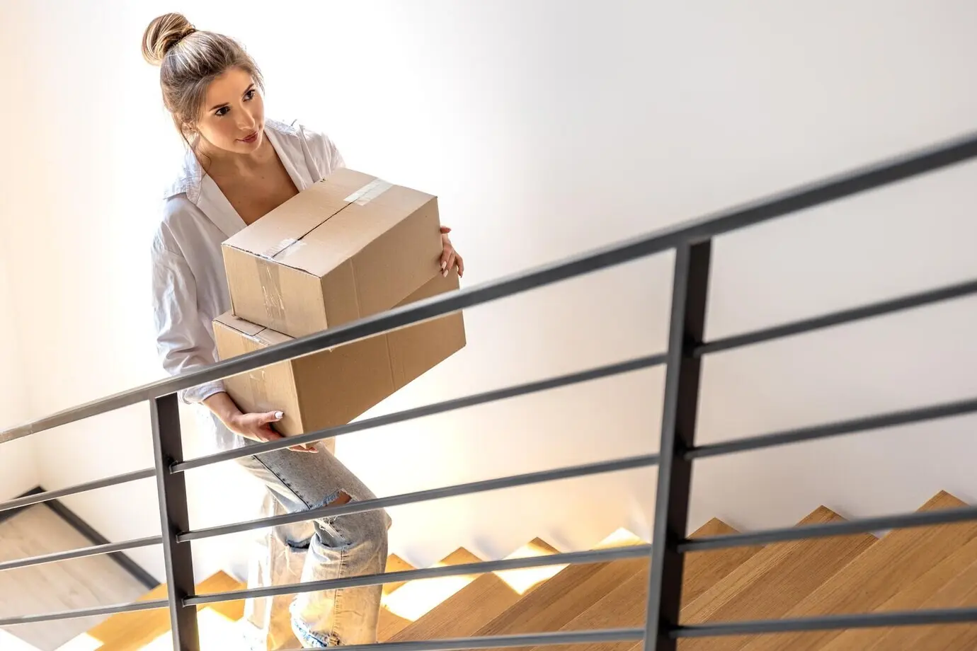 Junge Frau mit Paketen auf einer Treppe, in Draufsicht und mit diagonalen Linien, Online-Shopping.